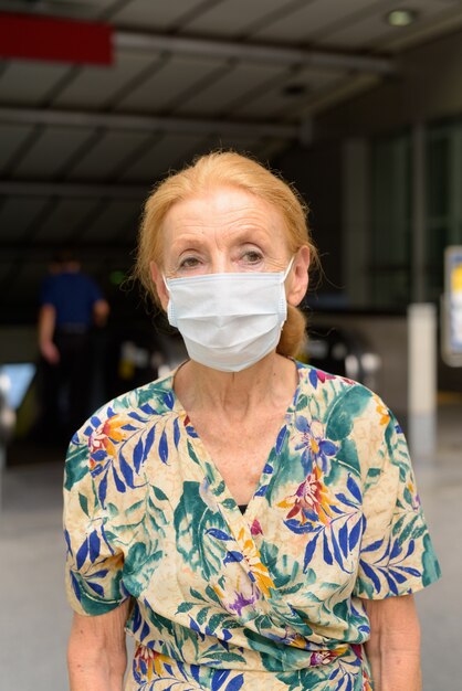 Mujer senior rubia con máscara pensando en la estación de tren de metro al aire libre