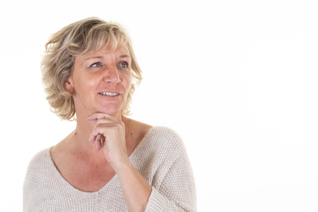 Mujer senior rubia de mediana edad hermosa madura con la mano bajo la cara dulce barbilla mirando hacia el lado sobre fondo blanco.