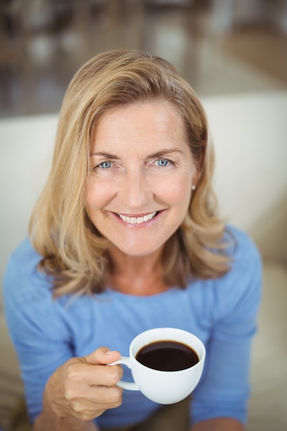 Mujer senior sonriente tomando una taza de café en la sala de estar