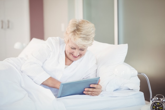 Mujer Senior con tableta digital mientras descansa en la cama