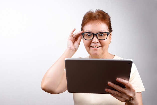 Mujer Senior en vasos con una tableta en blanco con una camiseta ligera