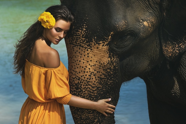 Mujer sensual en hermoso vestido naranja y poderoso elefante