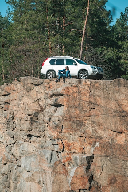 Mujer sentada en un acantilado con una hermosa vista en un coche suv de día soleado en el fondo