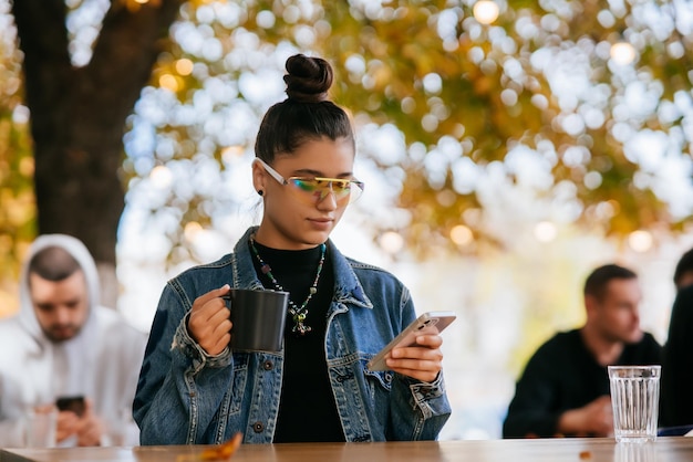 Mujer sentada al aire libre café bebiendo bebidas sosteniendo en la mano el teléfono inteligente