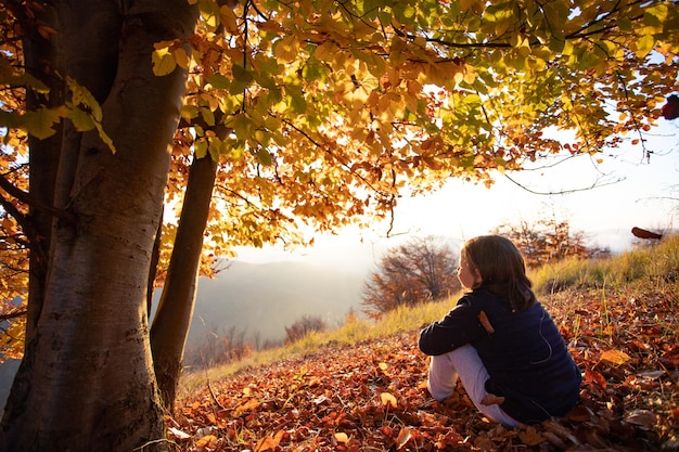 Foto mujer sentada en un árbol durante el otoño