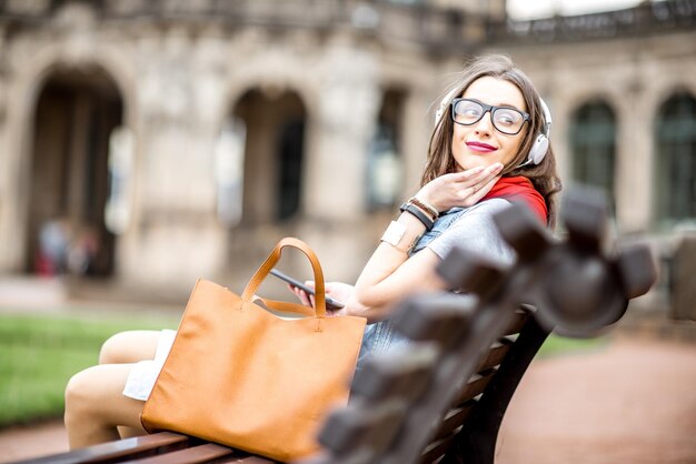 Mujer sentada con auriculares y bolsa en el banco en el casco antiguo de la ciudad de Dresde en Alemania