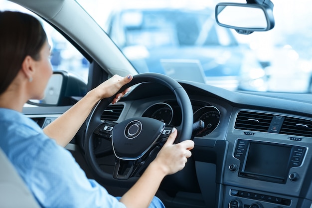 Mujer sentada en un auto nuevo en el salón del automóvil sosteniendo un volante