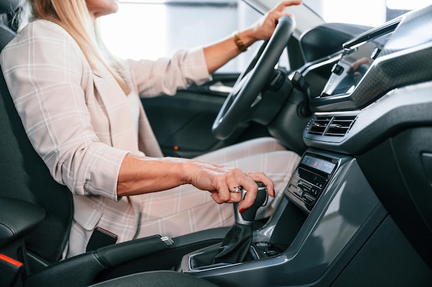 Mujer sentada en el automóvil con ropa formal blanca en el concesionario de automóviles