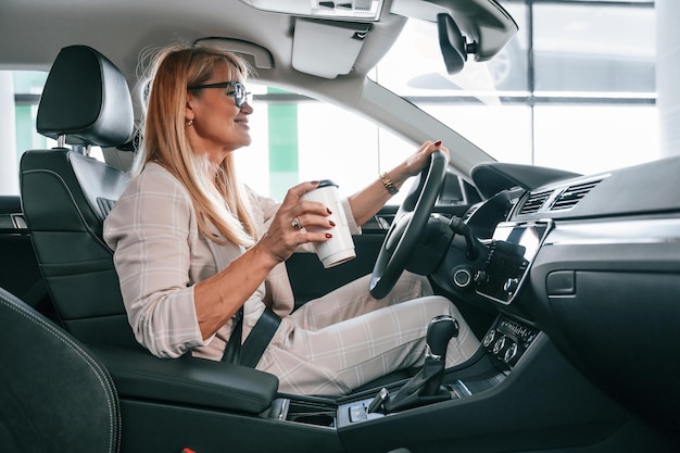 Mujer sentada en el automóvil con ropa formal blanca en el concesionario de automóviles