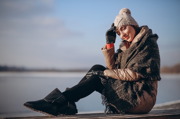 Mujer sentada en un banco junto al lago en invierno