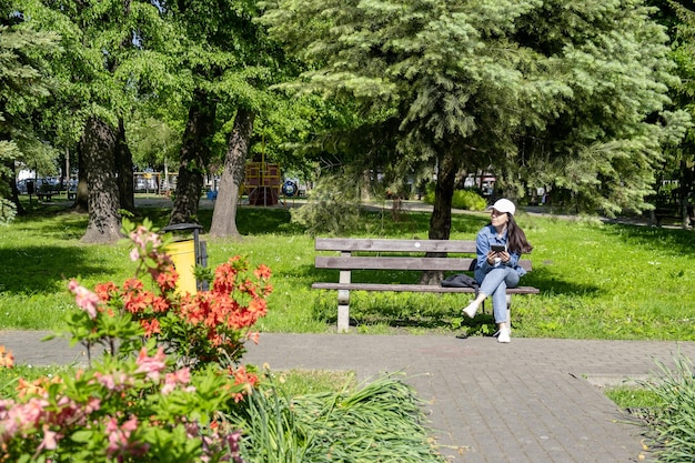 Mujer sentada en el banco en el parque público de la ciudad leyendo un libro electrónico