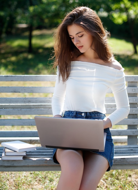 Mujer sentada en un banco en el parque y usando laptop