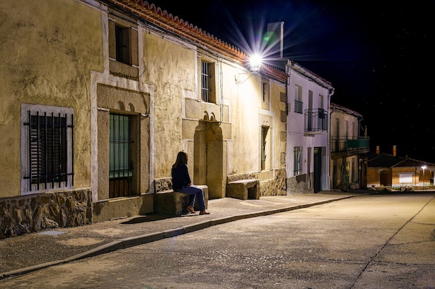 Mujer sentada en un banco de piedra en un antiguo pueblo por la noche.