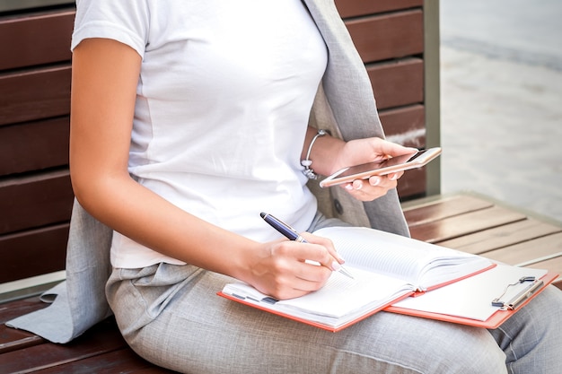 Mujer sentada en el banco con smartphone y bloc de notas