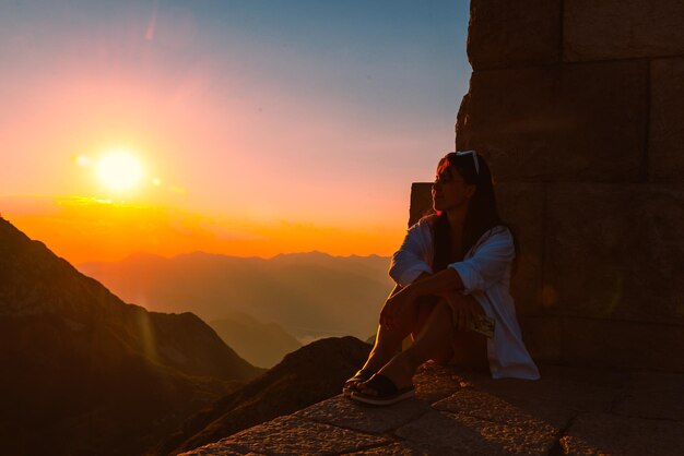 mujer sentada en el borde con una hermosa vista de la puesta de sol sobre las montañas