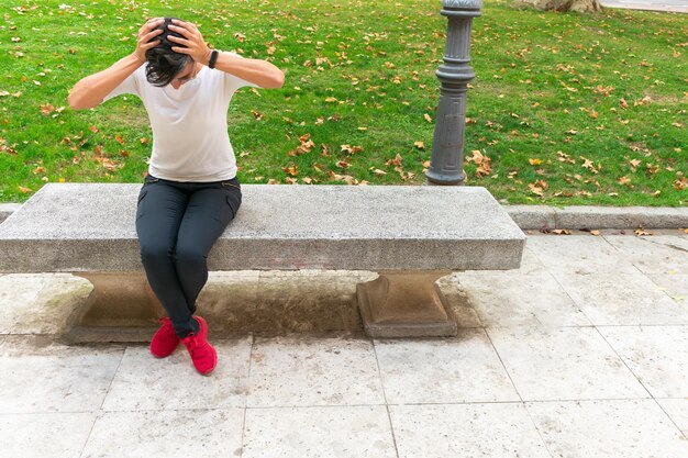 Foto mujer sentada con la cabeza en las manos en el banco