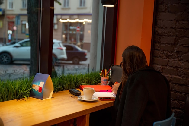 Mujer sentada en un café bebiendo té caliente trabajando dibujando al mismo tiempo