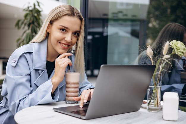 Mujer sentada en un café trabajando en una laptop y bebiendo café