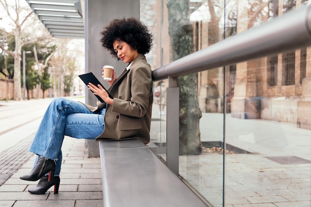 Mujer sentada con un café y usando una tableta