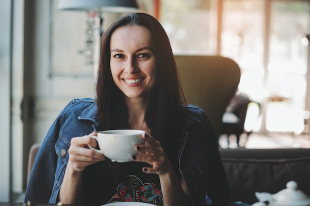 Foto mujer sentada en la cafetería con una taza de café y sonriendo