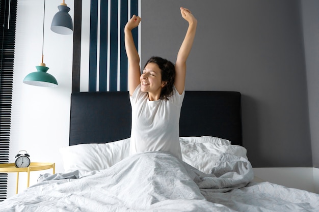 Foto mujer sentada en una cama con los brazos levantados