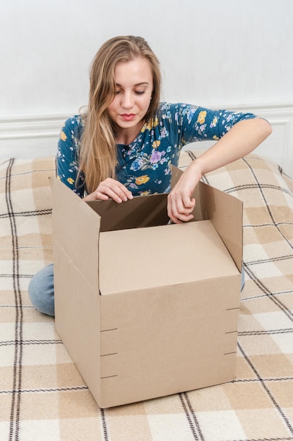 Mujer sentada en la cama desempacando una caja de cartón en casa Entregando un paquete