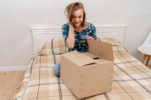 Foto mujer sentada en la cama desempacando una caja de cartón en casa entregando un paquete