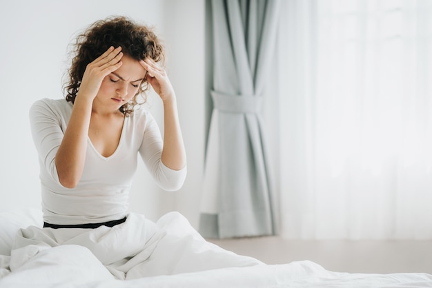 Mujer sentada en la cama sintiendo dolor de cabeza