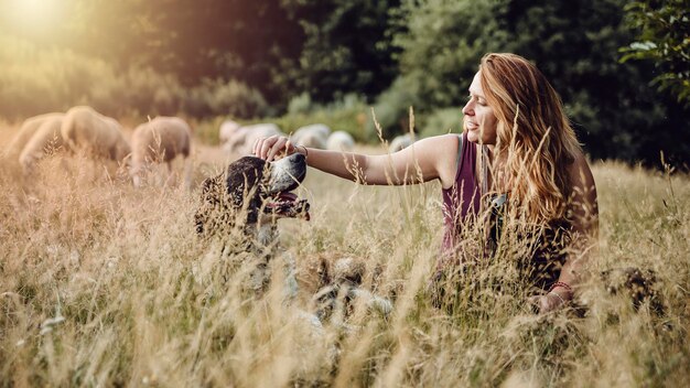 Mujer sentada en un campo acariciando a un perro pastor