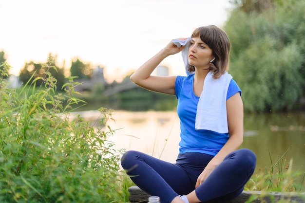 Mujer sentada cansada después del tiempo de fitness en el parque de la ciudad