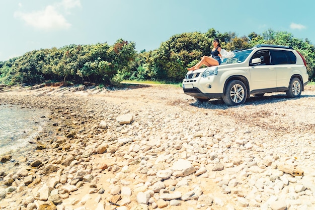 Mujer sentada en el capó del coche en el concepto de vacaciones de verano en la playa