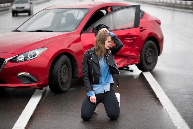 Mujer sentada en la carretera después de un accidente. Mujer herida que se siente mal después de un accidente automovilístico