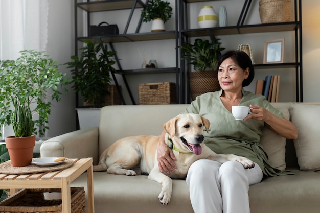 Mujer sentada en casa en el sofá tomando una taza de café al lado de su perro