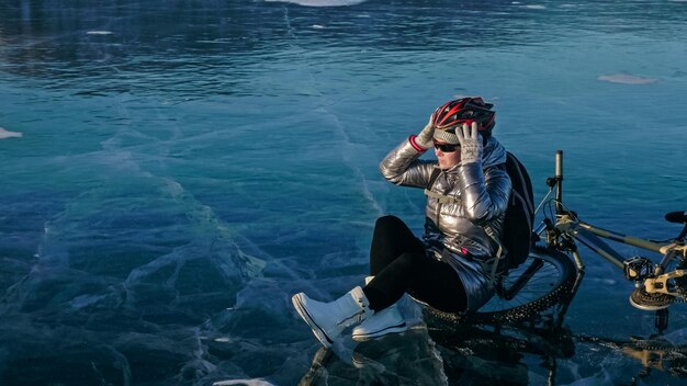 Mujer sentada cerca de su bicicleta en el hielo La niña ciclista se detuvo para descansar Se sienta en el volante y disfruta de la hermosa vista de la puesta de sol El viajero está montando un ciclo La mujer está montando en bicicleta en el hielo