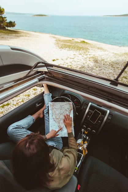 Mujer sentada en el coche comprobando el mapa de la playa del mar en el fondo. concepto de vacaciones de verano