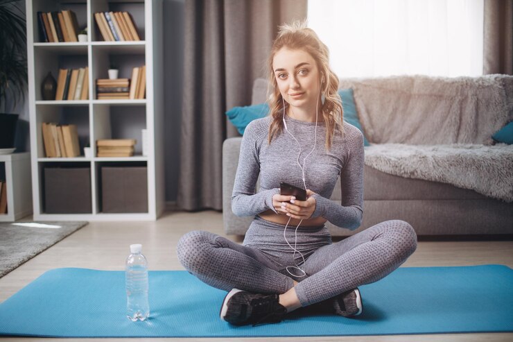 Mujer sentada en una colchoneta de yoga con teléfono inteligente y auriculares