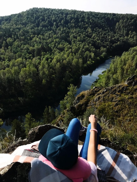 Foto mujer sentada contra una montaña de árboles en un acantilado