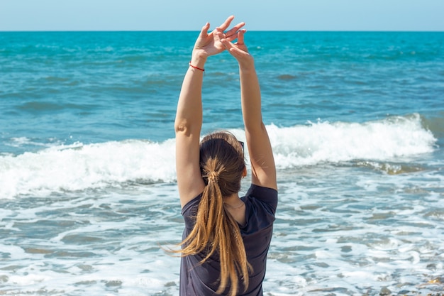 mujer sentada en la costa levantando las manos