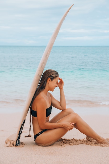 Una mujer sentada debajo de una tabla de surf.