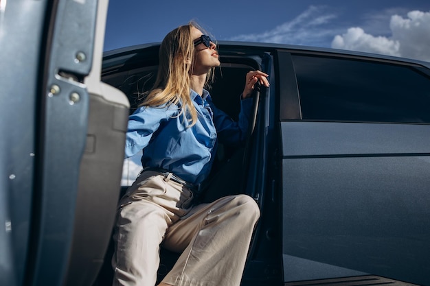 Mujer sentada dentro de su coche eléctrico con la puerta abierta