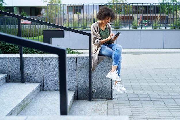 Mujer sentada en las escaleras de la ciudad y desplazándose por el teléfono