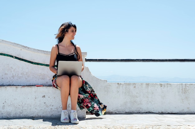 Mujer sentada escribiendo con laptop cerca del mar