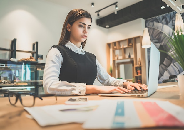 La mujer sentada en el escritorio cerca de papeles y una computadora portátil