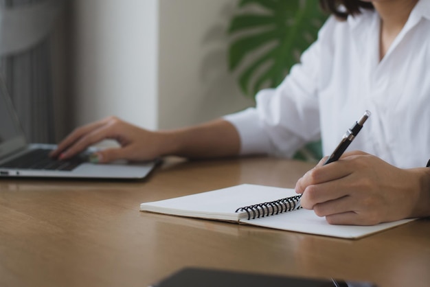 Mujer sentada en un escritorio con computadora portátil y tomando notas en un cuaderno