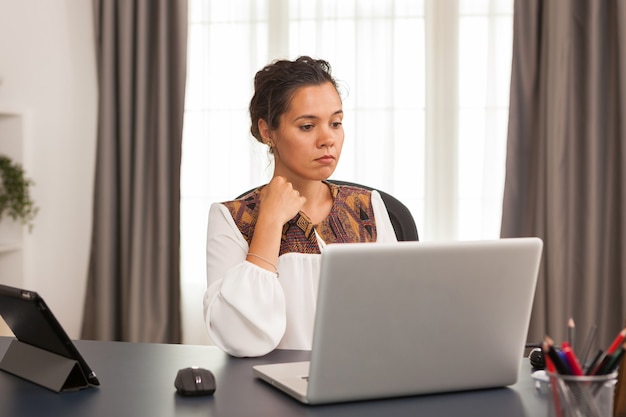 Mujer sentada en el escritorio en la oficina en casa trabajando de forma remota en la computadora portátil.