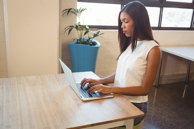 Mujer sentada en el escritorio y trabajando en la computadora portátil