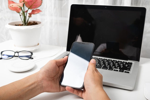 Foto mujer sentada en el espacio de trabajo usando la mano sosteniendo una pantalla en blanco de teléfono inteligente negro en una mesa con una computadora portátil mujer sosteniendo un teléfono móvil con un cuaderno en la oficina