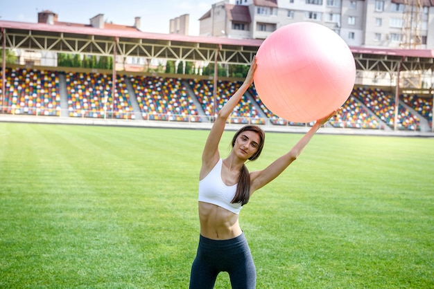 Mujer sentada en fitball. Mujer joven y deportiva entrenando al aire libre