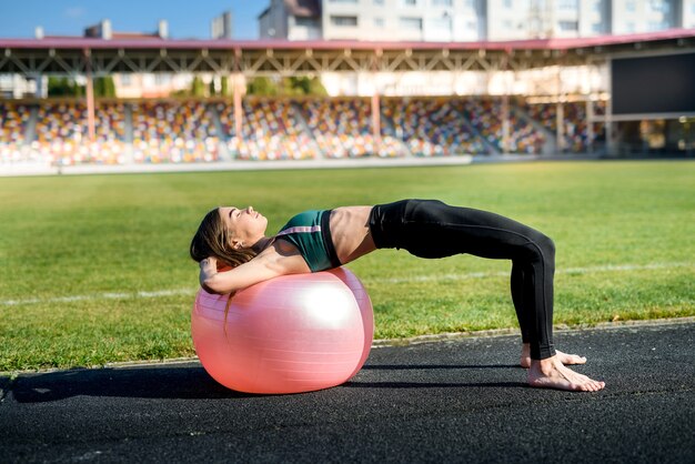 Mujer sentada en fitball. Mujer joven y deportiva entrenando al aire libre