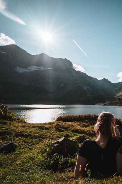 Foto mujer sentada frente a una montaña y un lago con cielo azul